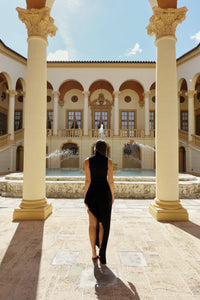 ARI Black Dress with ruffles and turtle neck in an elegant courtyard setting.